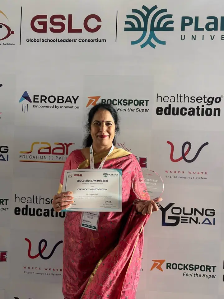 A KIS educator holding her award certificate in front of the sponsors’ wall