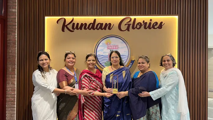 The Principal and five teachers holding the award in front of the Kundan Glories wall