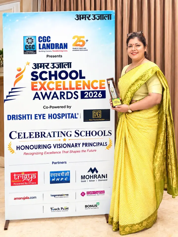 A KIS educator with the trophy beside the Amar Ujala School Excellence Awards 2026 standee